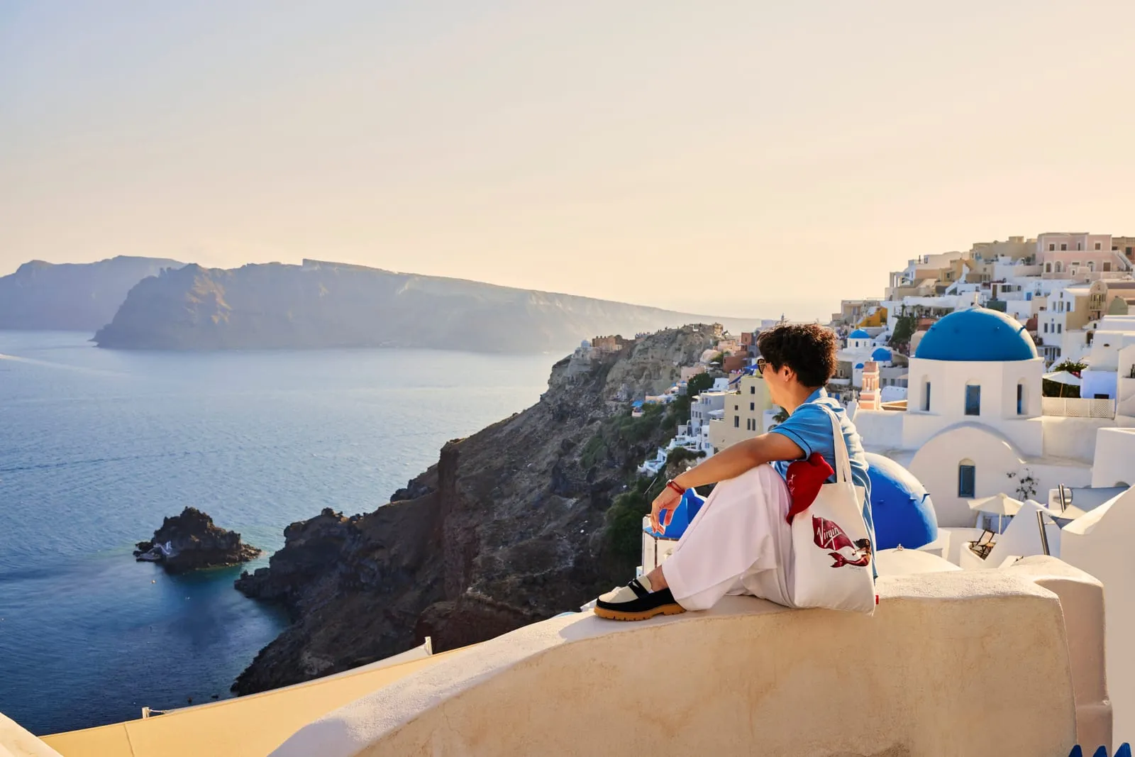Santorini at golden hour — a solo traveler taking in the view above Fira and Oia