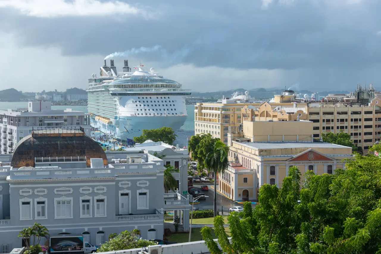 A large cruise ship moored in a vibrant urban harbor, surrounded by historic architecture.
