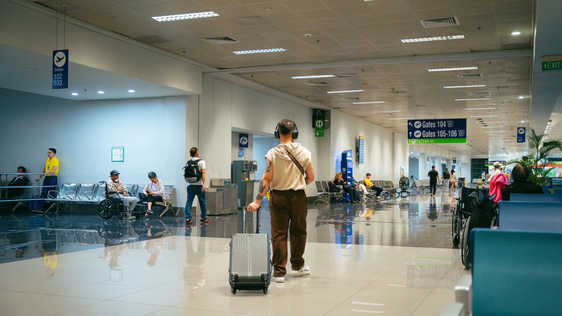 An airport departures hall with travelers walking and seated, including passengers using wheelchairs