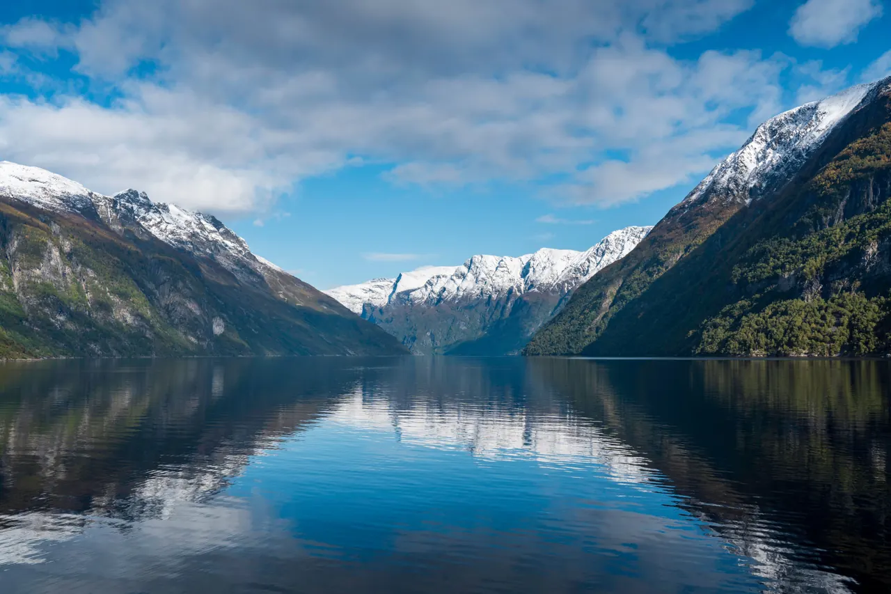 Serene Norwegian fjord with mountains and reflections on a clear day.