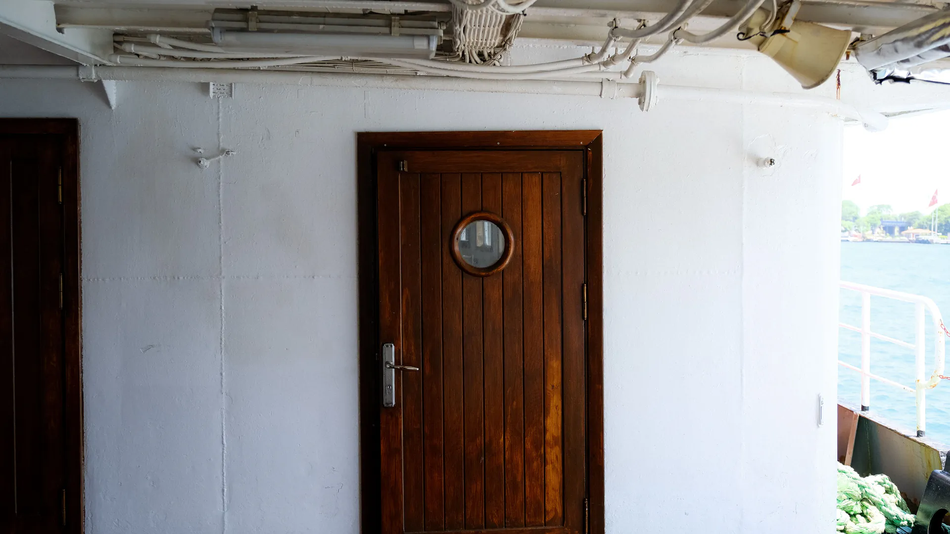 A heavy wooden door with a brass porthole set into a ship's deck bulkhead