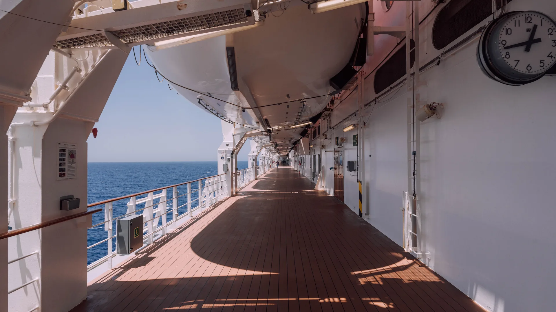 A wide, empty cruise ship promenade deck with the ocean beyond the railing