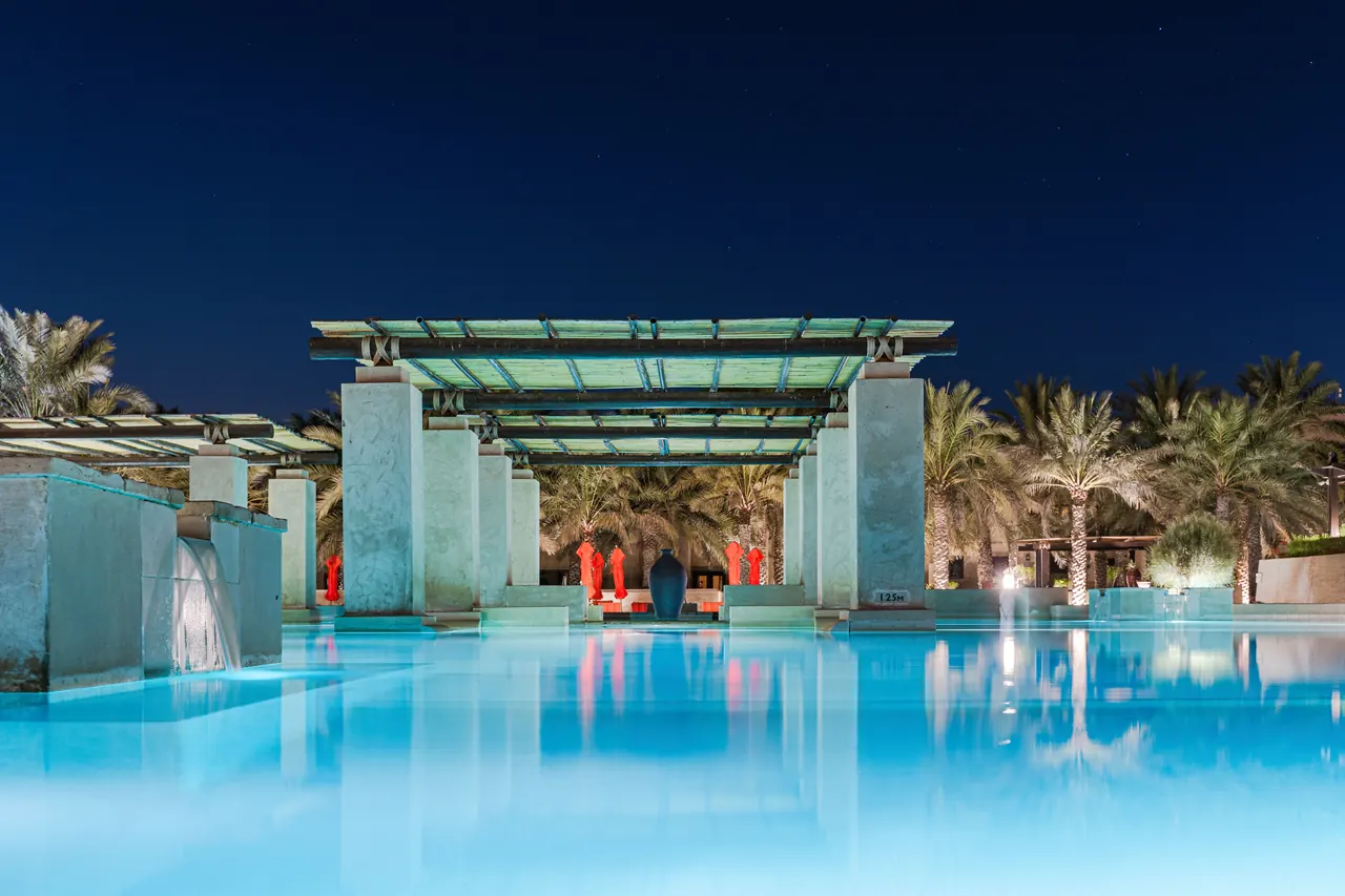 Stunning view of a serene hotel pool surrounded by palm trees at night in Dubai.