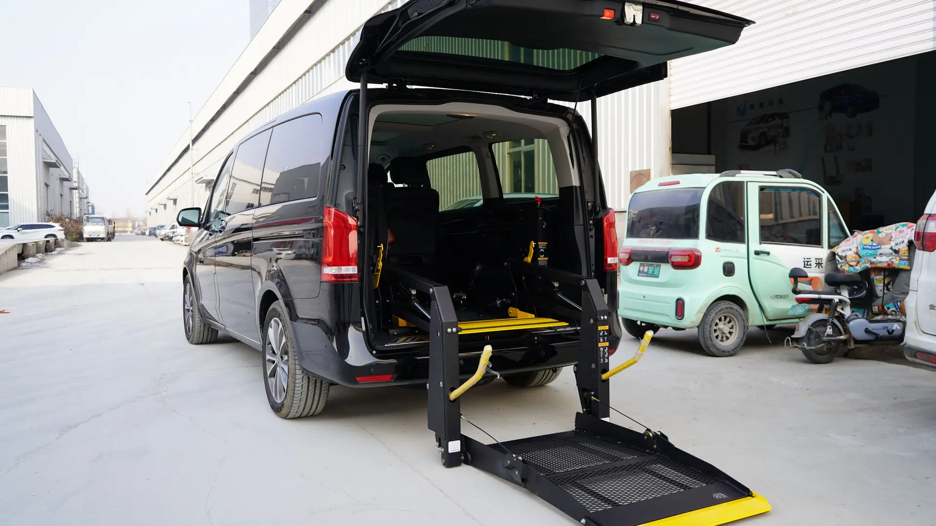 A dark van parked on a city street with its rear hydraulic wheelchair lift lowered to the pavement