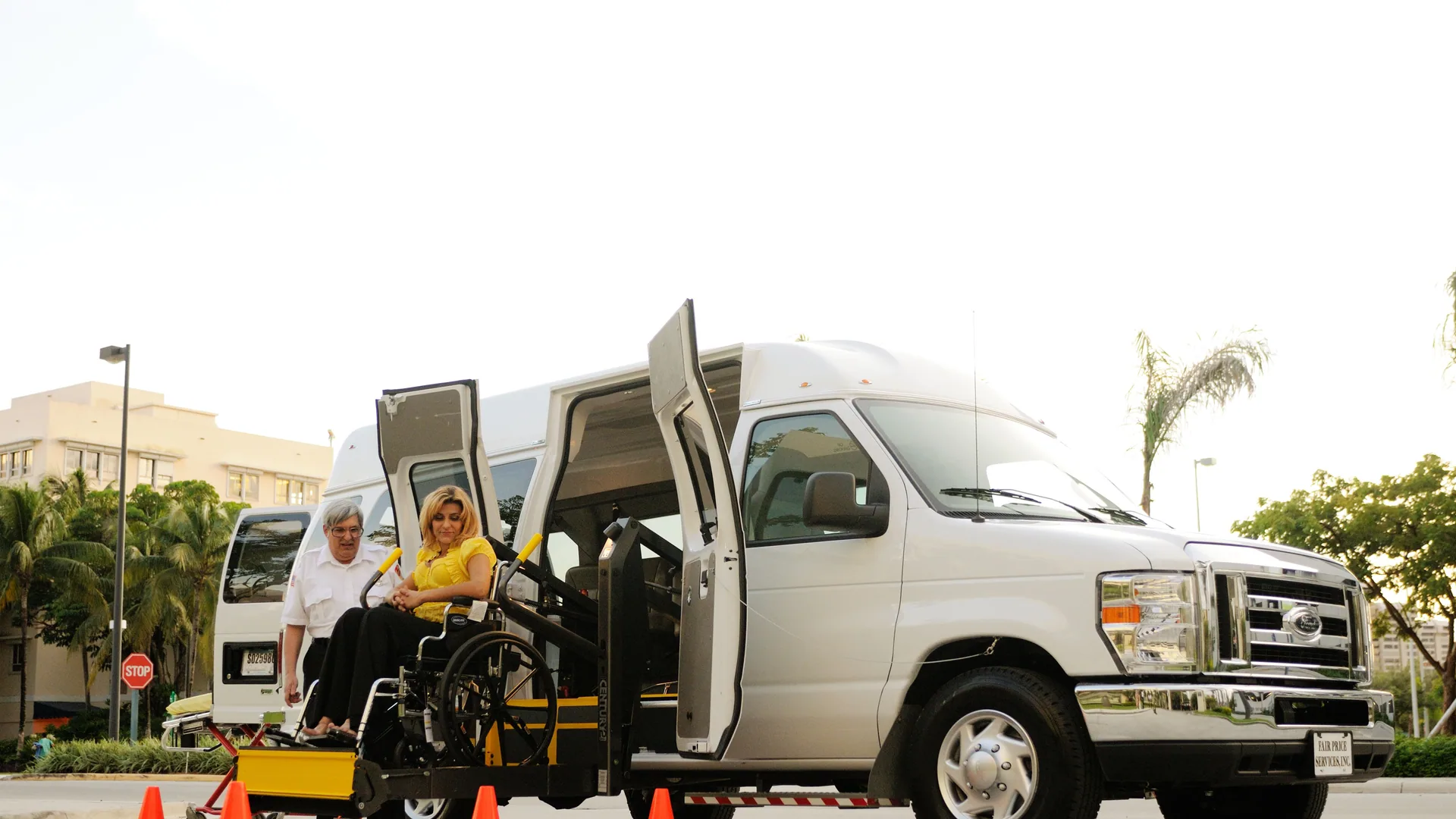 A wheelchair user boarding an adapted van on a hydraulic lift, assisted by the driver