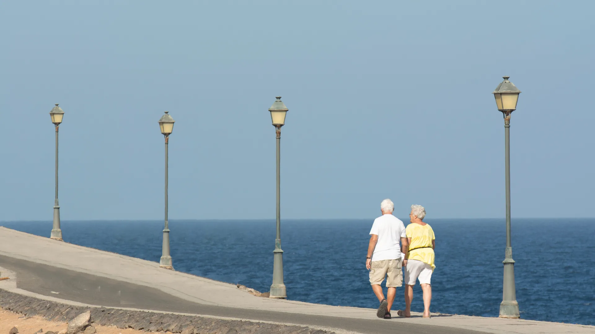 An older couple walking together along a seaside promenade on a calm day