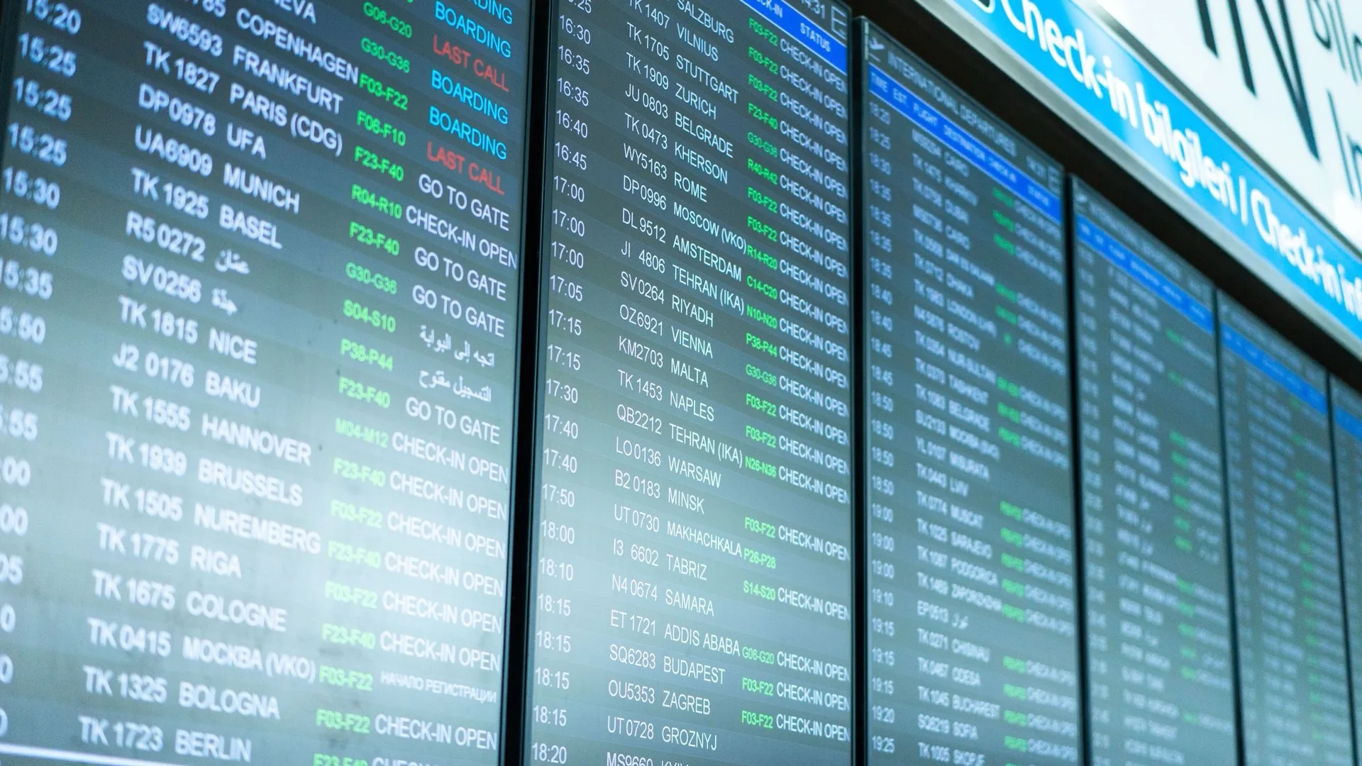 Airport departure boards showing flight numbers, gates and boarding statuses