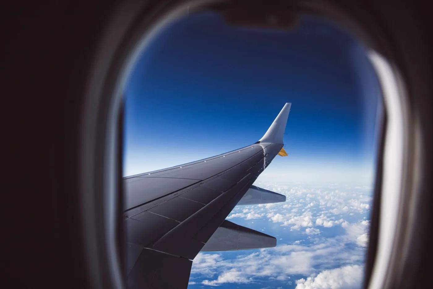 A wing and cloud deck seen through an aircraft cabin window in daylight