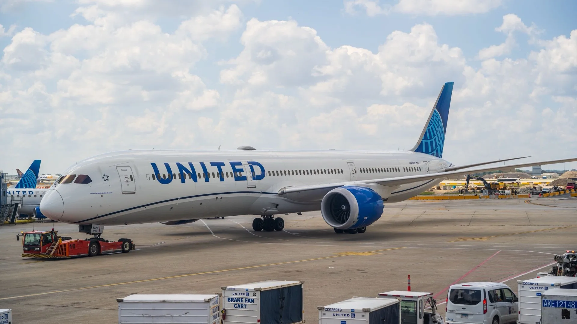A United Boeing 787 Dreamliner on stand at a busy airport under a cloudy sky