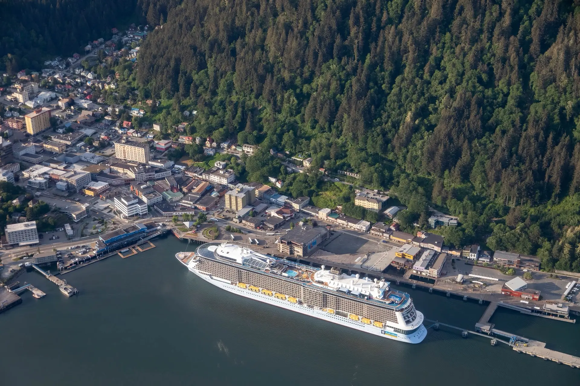 Aerial view of a large cruise ship berthed alongside downtown Juneau, Alaska, the vessel roughly the length of the town's waterfront