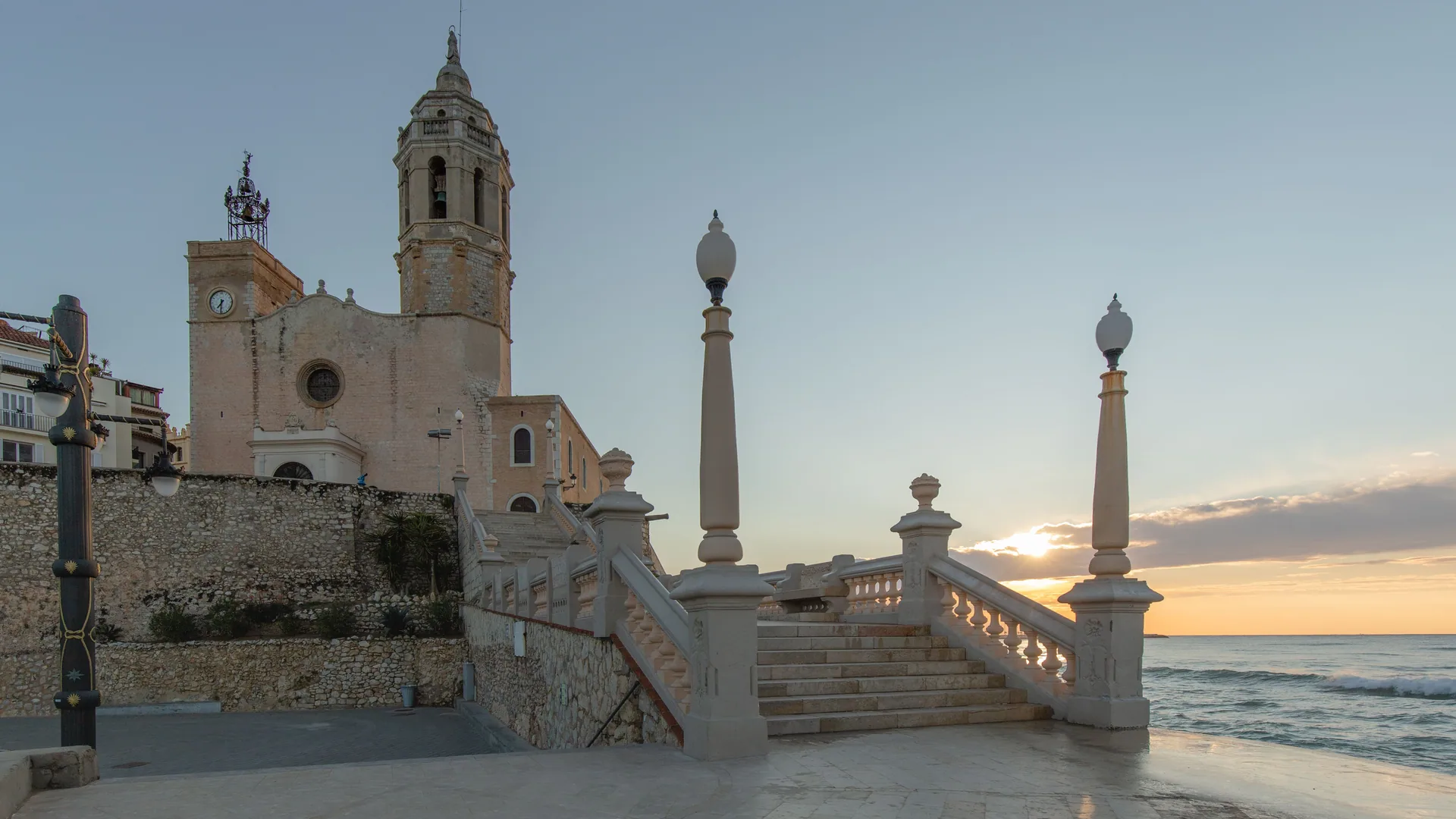 The church of Sant Bartomeu above the Sitges seafront at sunrise, with steps down to the promenade