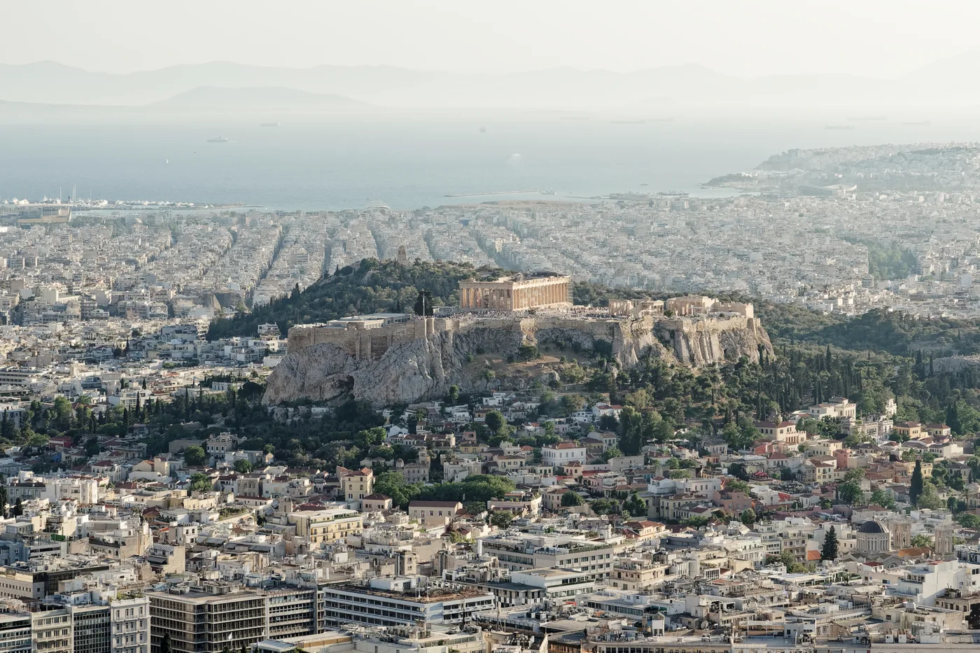 The Acropolis above Athens at golden hour, with the Saronic Gulf and Piraeus beyond