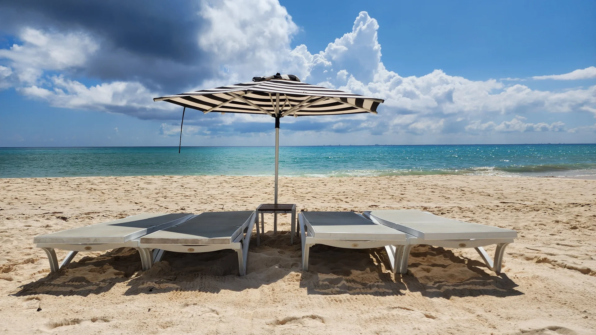 Empty sun loungers under a striped parasol on a quiet Caribbean beach