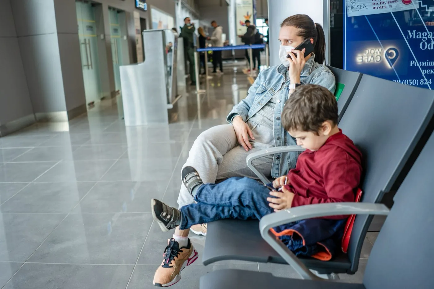 An adult and a child waiting together in an airport terminal seating area