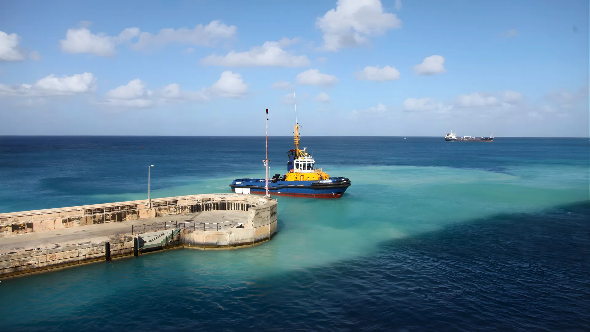 A tugboat moored at a dock in clear blue water under a bright sky