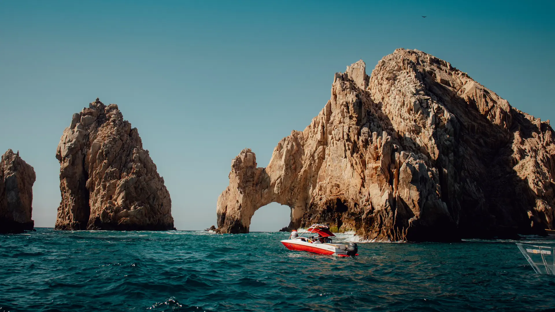 A small boat passing the towering El Arco rock formation at Land’s End in Cabo San Lucas under a teal sky