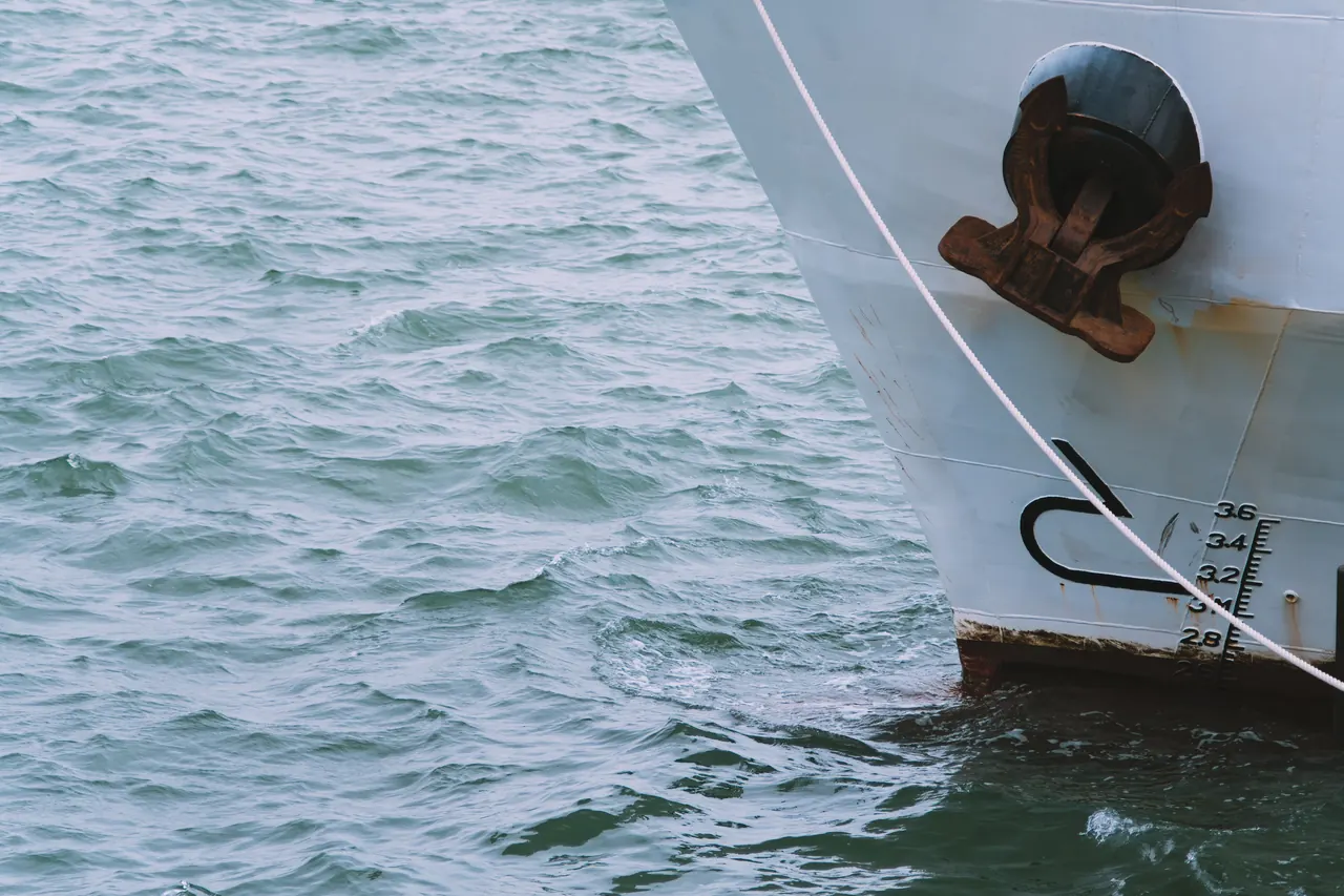 A detailed view of a ship’s bow and anchor slicing through vibrant aqua waves.