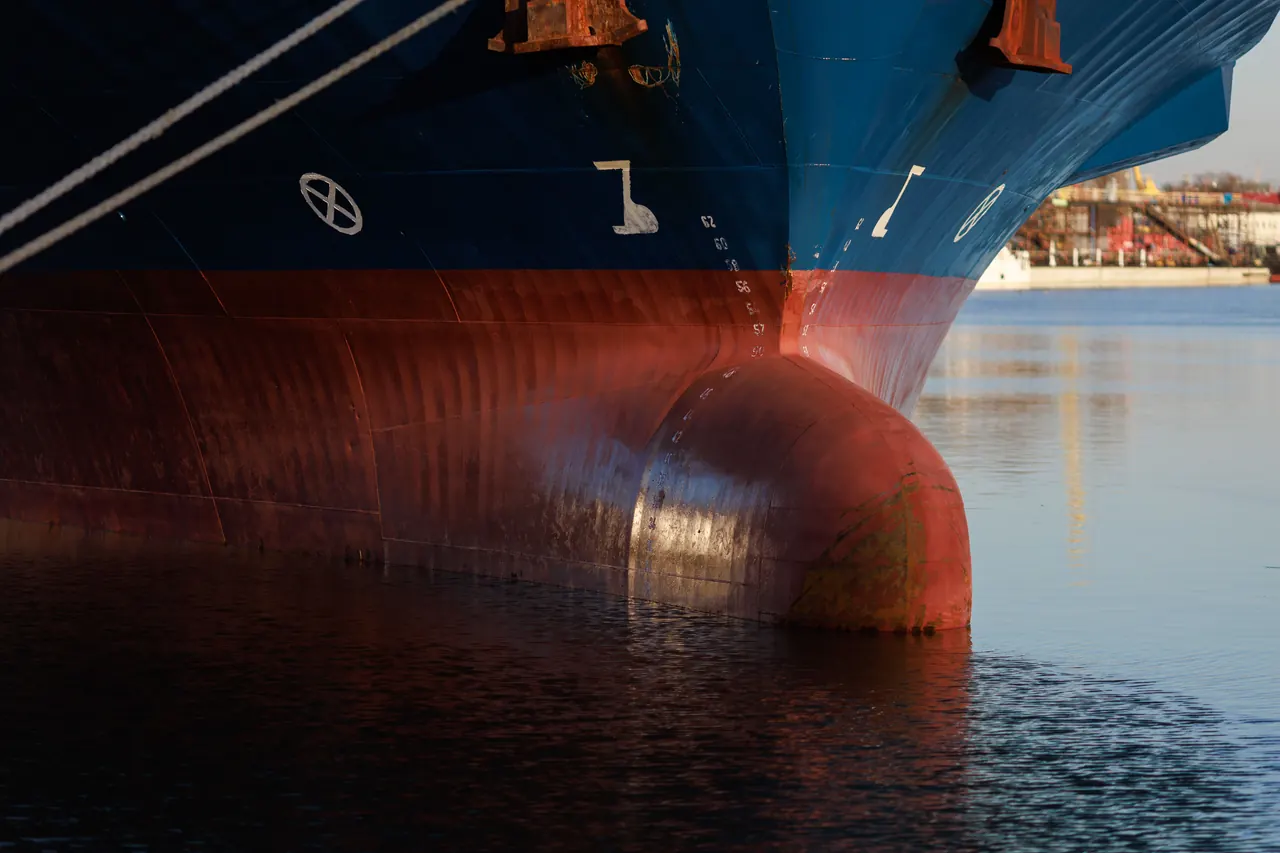 Close-up of cargo ship bow in industrial harbor reflecting on calm water.
