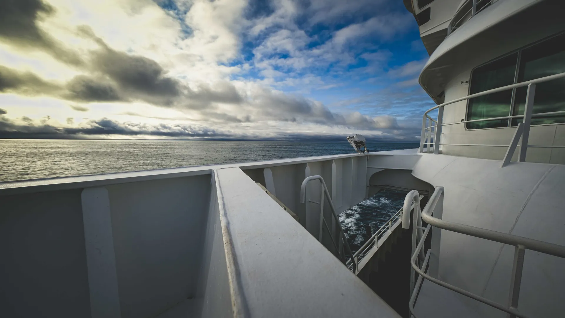 Ship deck rails and open ocean under a broken sky