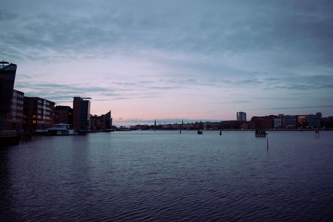Panoramic view of Copenhagen’s waterfront skyline at dusk featuring urban buildings and calm sea.