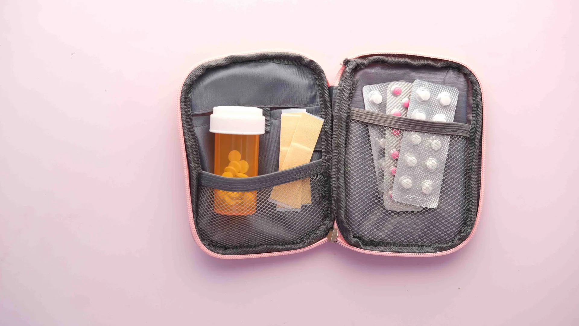 An open travel medical kit with a labeled pill bottle, blister packs and dressings