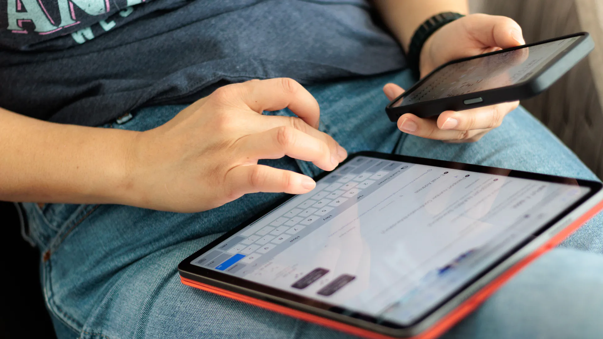 A person's hands using a tablet and a smartphone side by side