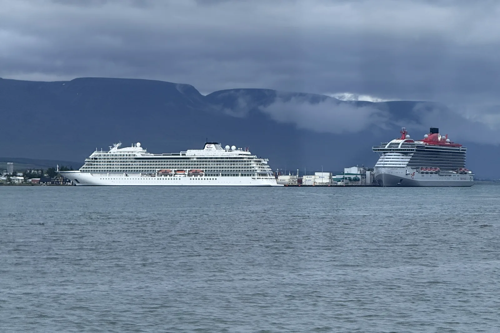 A Viking ship and a Virgin Voyages ship alongside at Akureyri, Iceland, under low cloud with mountains behind