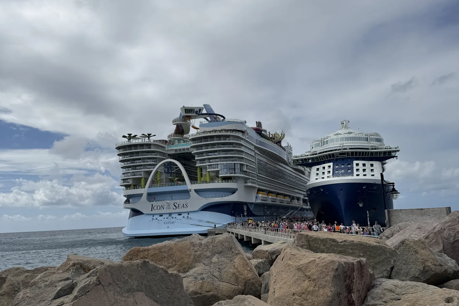 Icon of the Seas and another large cruise ship berthed together at St Kitts, with guests filing along the pier