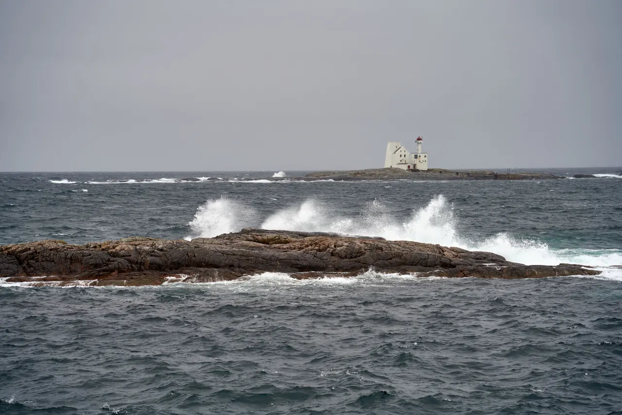 Waves crashing on rocks near a picturesque lighthouse in coastal Norway.