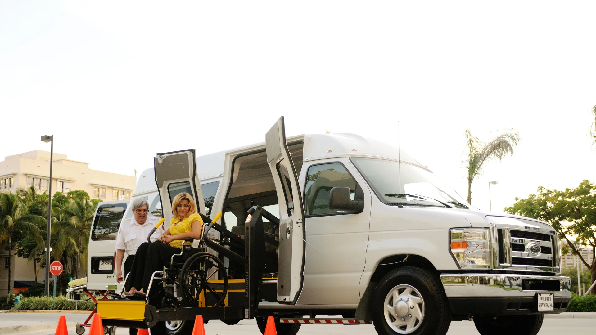 A woman using a wheelchair boarding an accessible van by lift, assisted by the driver
