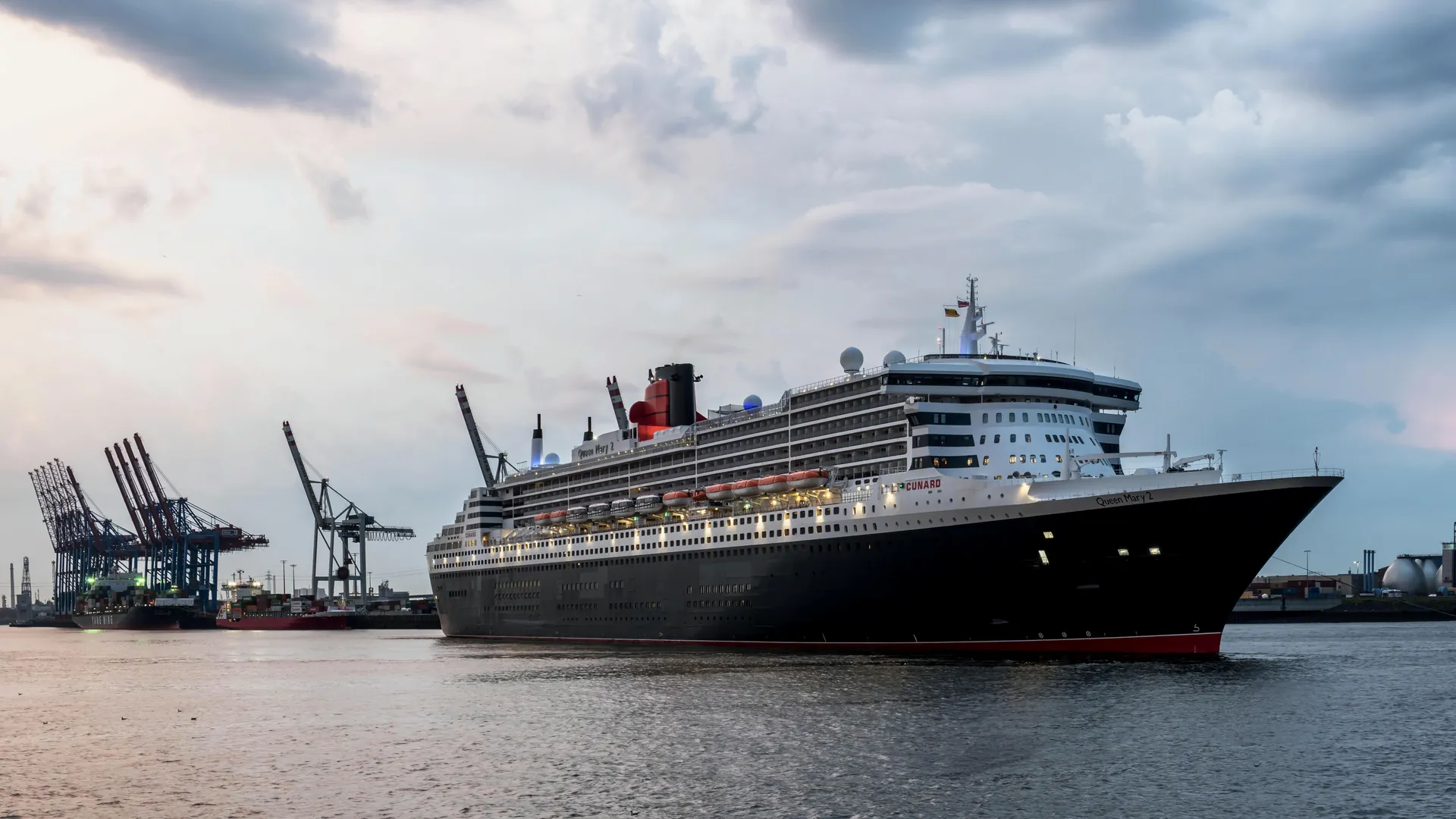 Queen Mary 2 moored at Hamburg harbor under a morning sky, with cranes along the quay