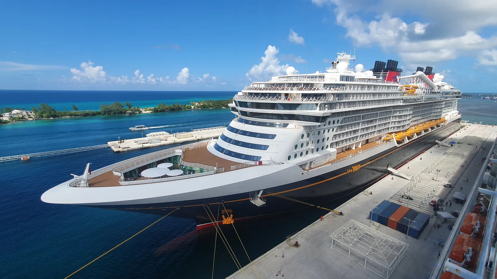 The Disney Wish alongside in port, her dark blue hull and twin yellow funnels filling the frame under a bright sky