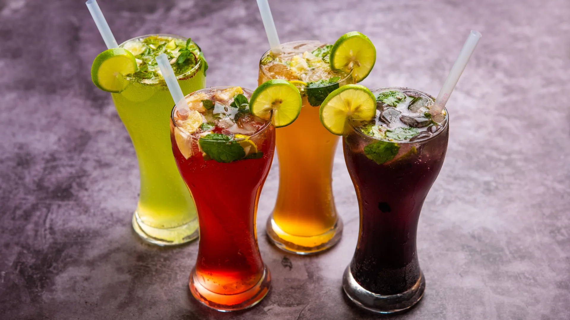 Four tall soft drinks garnished with lemon and mint, served with straws