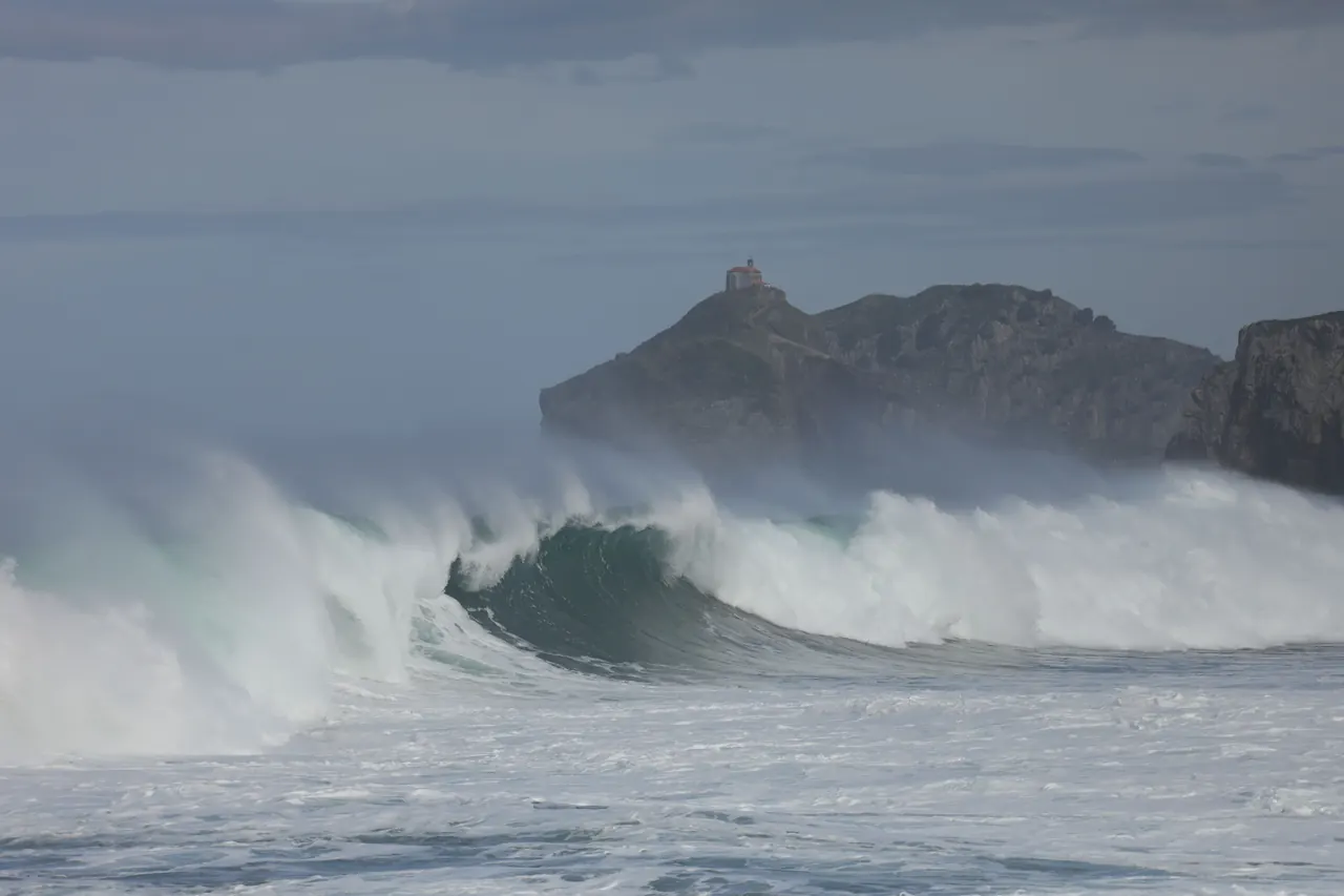 Powerful ocean waves crashing onto Bakio’s rugged coastline under cloudy skies.