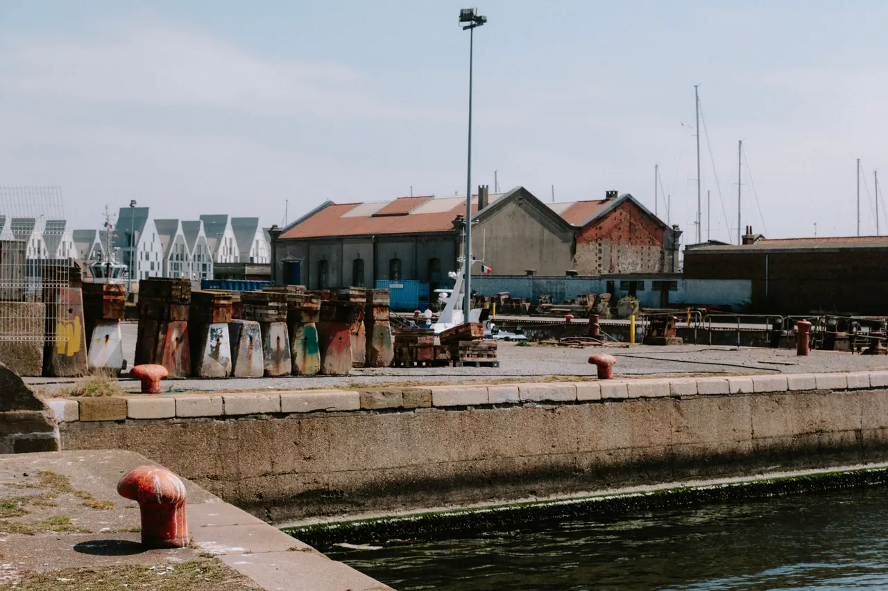 Explore an industrial harbor scene with aged buildings and colorful quay structures under a clear sky.