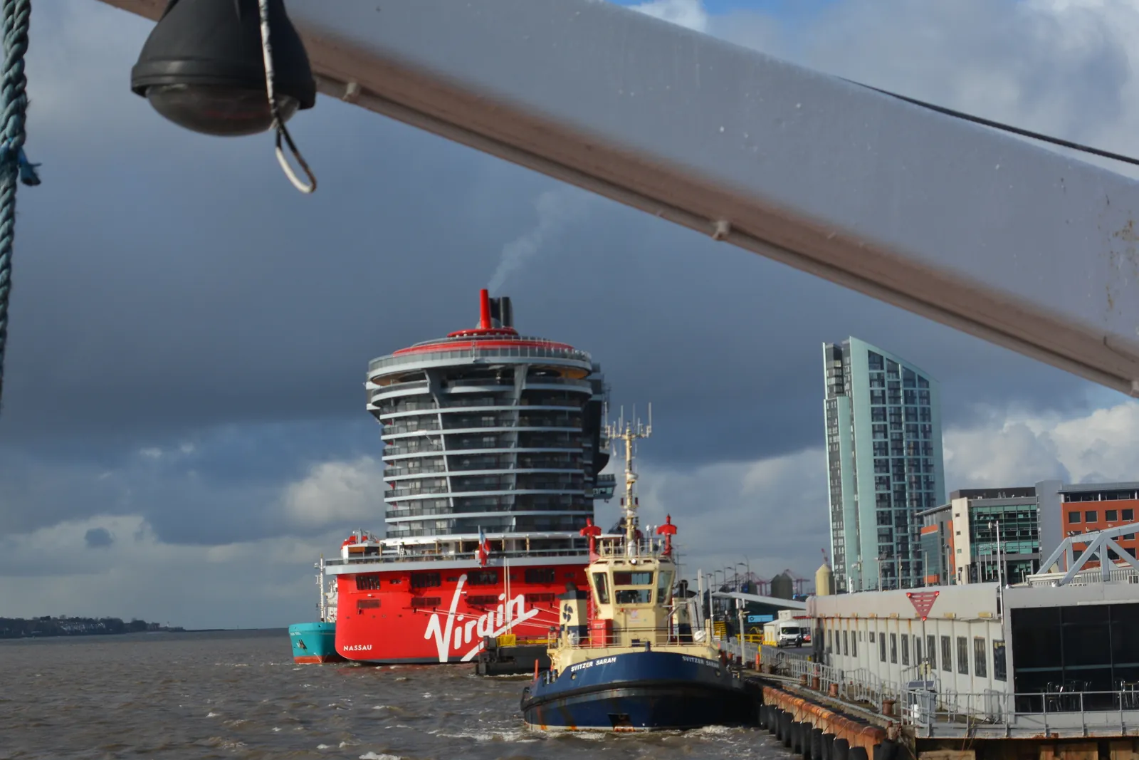 Virgin Voyages' Scarlet Lady seen from astern, her red-accented hull and tiered aft decks rising above the water