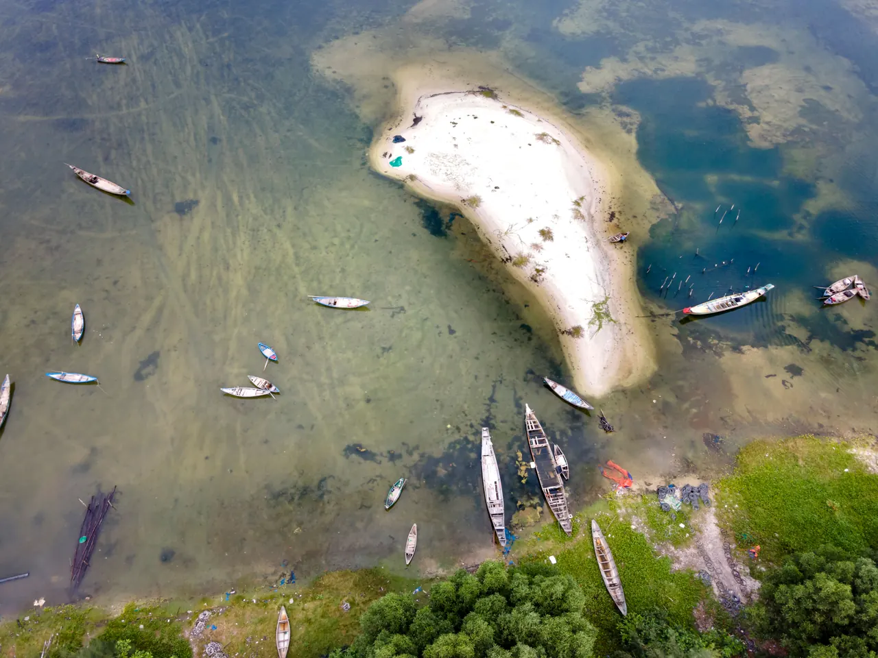 Aerial shot of boats surrounding a small sandy island in clear waters.