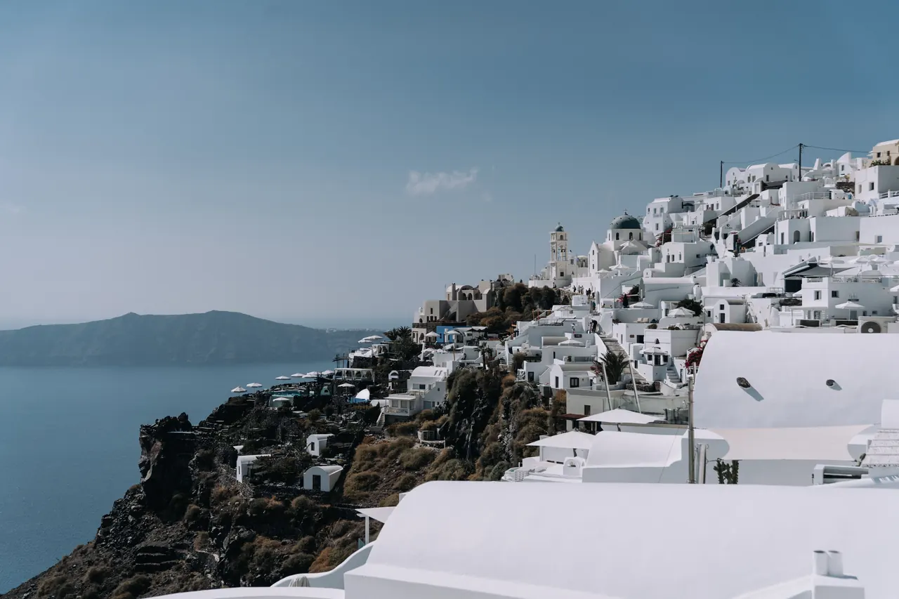 A breathtaking view of Santorini’s whitewashed buildings cascading down a cliff overlooking the Aegean Sea.