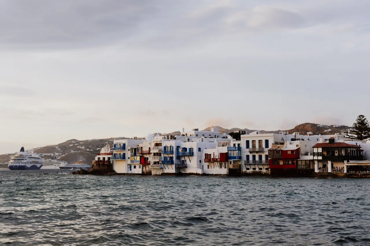 Charming seaside view of the iconic Little Venice in Mykonos, Greece with a cruise ship in the background.