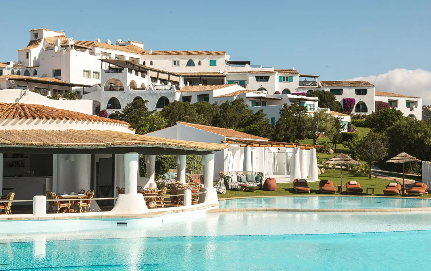A whitewashed hillside resort with cabanas and a restaurant above a turquoise bay on Costa Smeralda, Sardinia