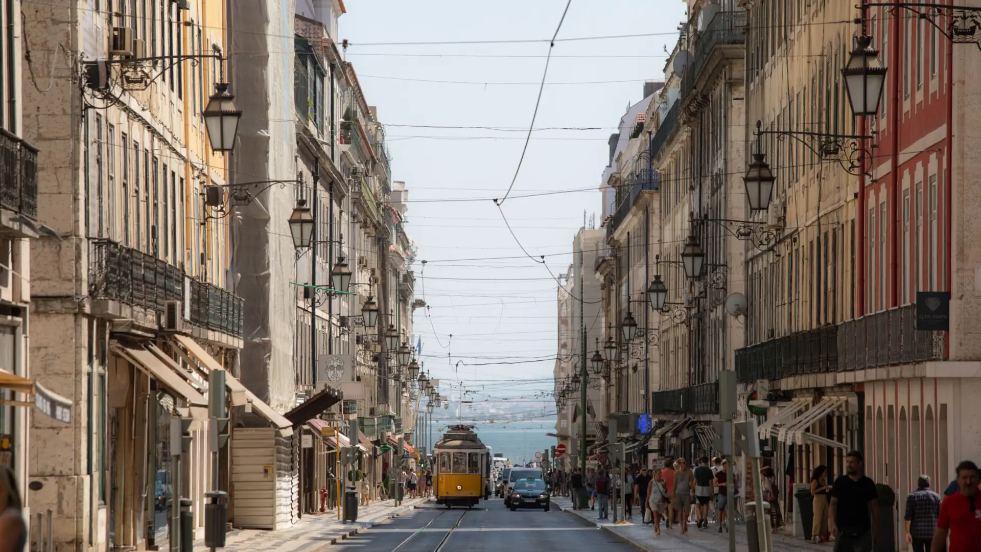A classic yellow tram coming down a long straight Lisbon street lined with tall historic buildings and pedestrians