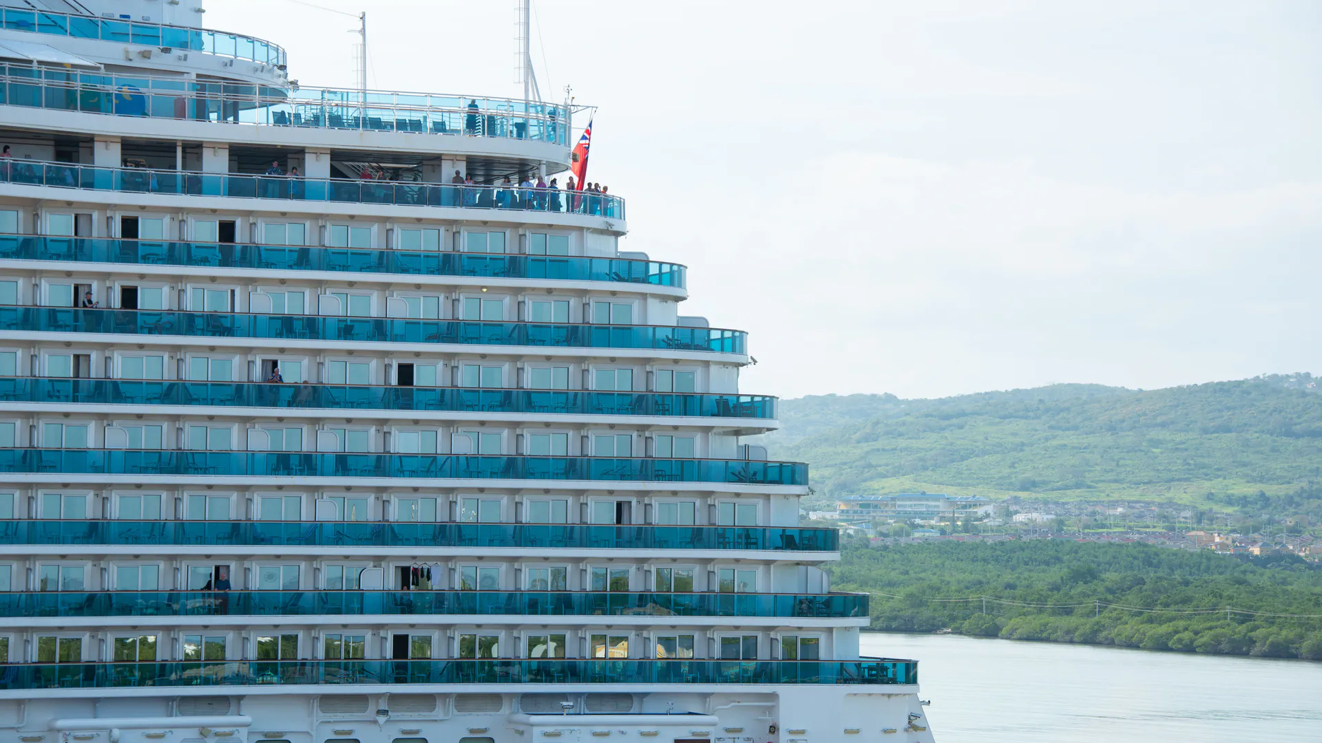 The tiered balcony decks of a large cruise ship rising above a green coastline