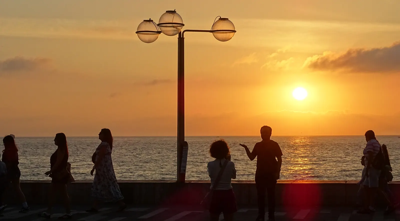 Sunset along the Malecón at Mazatlán, the seafront promenade curving away beneath an orange sky