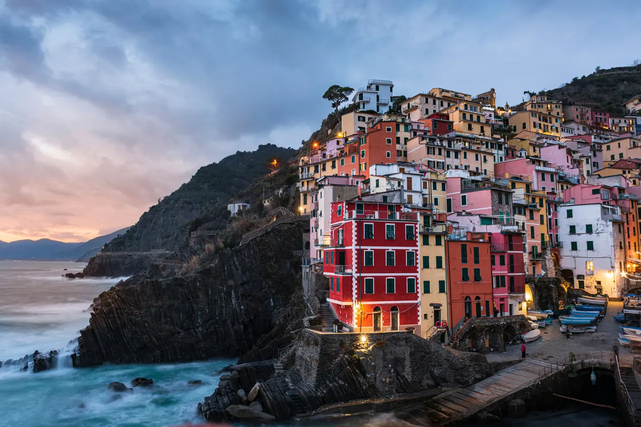 Scenic view of Riomaggiore’s vibrant houses on a cliffside at sunset, Liguria, Italy.