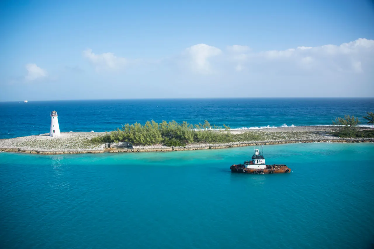 A quiet Bahamian shoreline with a lighthouse and a small working boat on calm water