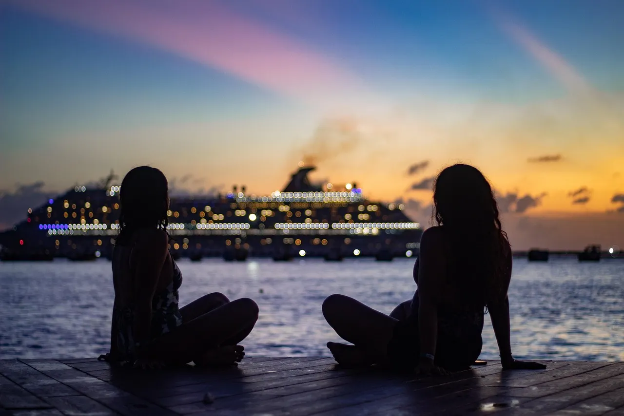 An empty curved teak promenade deck of a cruise ship at sunset, looking out over a calm ocean