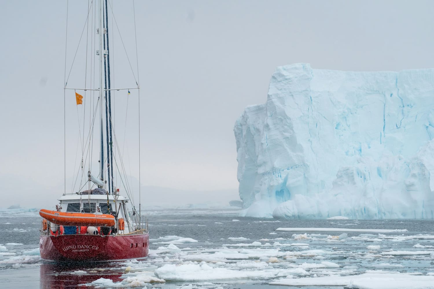 An expedition vessel in pack ice beside a massive iceberg in polar waters