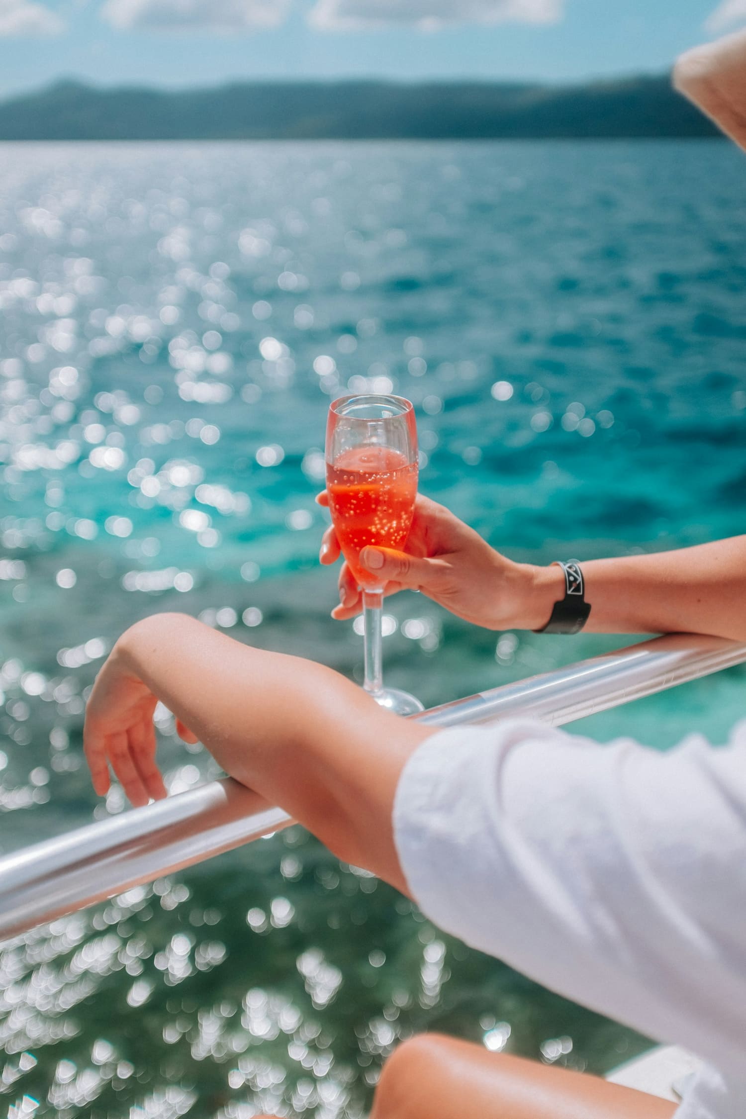 A guest at a ship's railing holding a sparkling drink over turquoise water