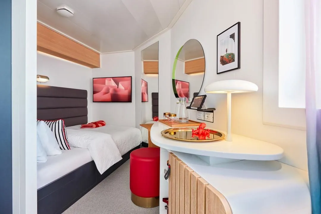 A Virgin Voyages Solo Sea View cabin interior showing a queen bed, round mirror, vanity area and bright natural light through the sea-view window