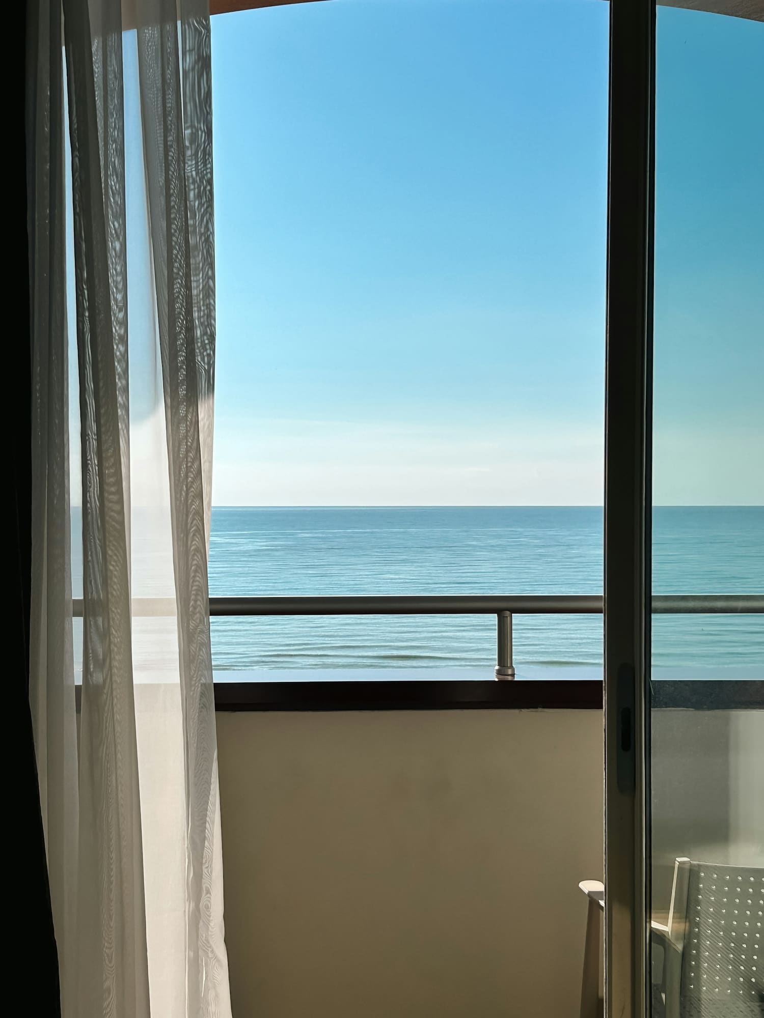 An airy cabin balcony with a sheer curtain and an open ocean view